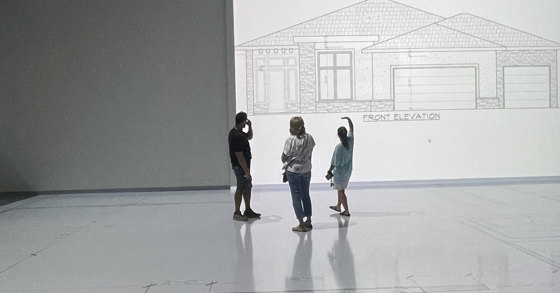 Clients walking a front elevation projected at full scale in the studio